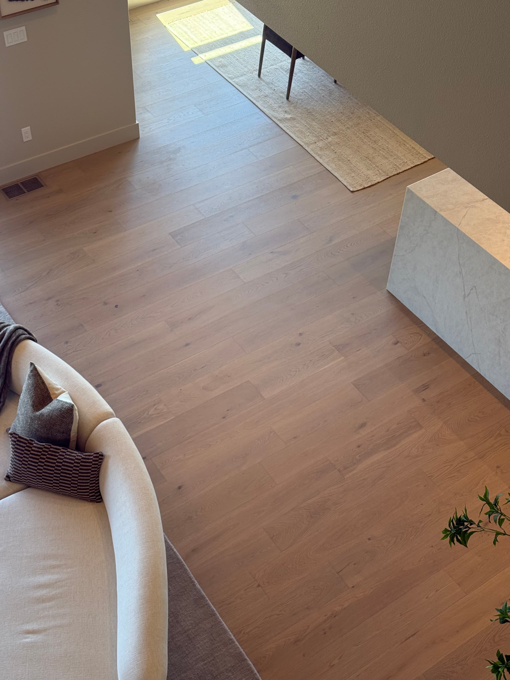 Overhead view of wide-plank engineered hardwood flooring running from the living room past a marble waterfall island into the dining area with a jute runner — Skyview Flooring project in Bethany, OR