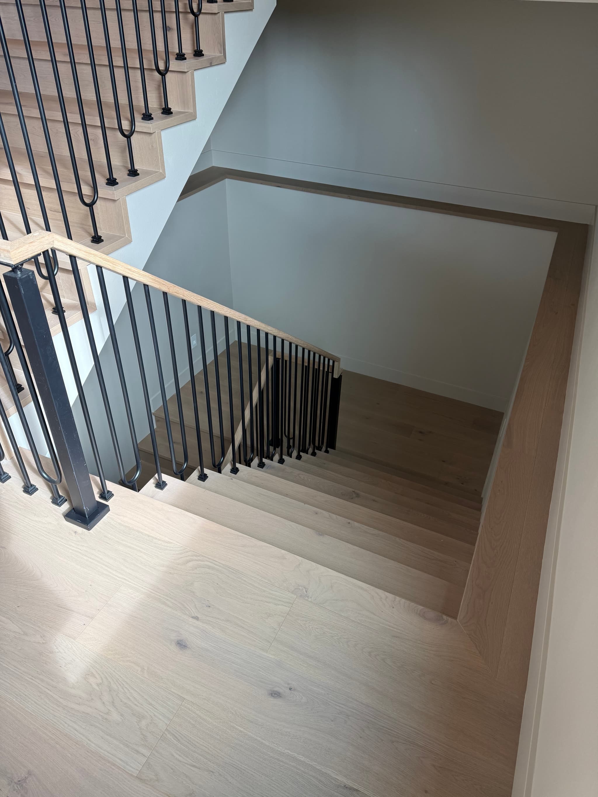 Light oak engineered hardwood staircase with black iron balusters and matching landing — Skyview Flooring project in Bethany, OR