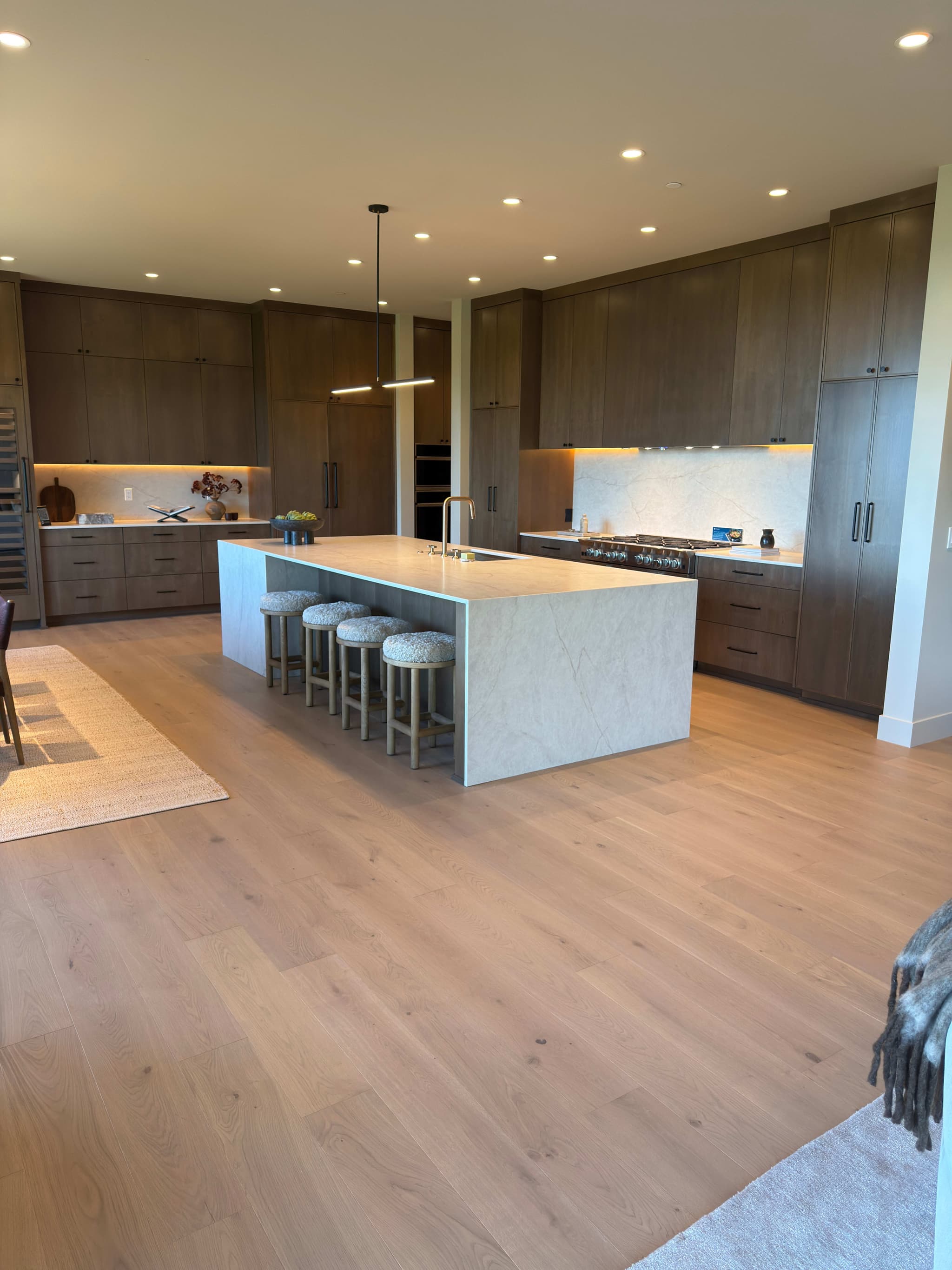 Wide-plank engineered white oak hardwood flooring in an open-concept kitchen with a long marble waterfall island, boucle bar stools, and dark stained cabinetry — Skyview Flooring project in Bethany, OR