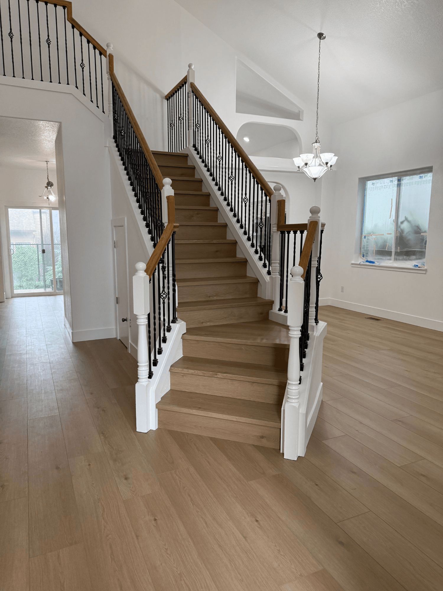 LVP luxury vinyl plank staircase installation with white-painted risers and newel posts, black wrought-iron balusters, and an oak handrail cap, in a home still under construction — Skyview Flooring project