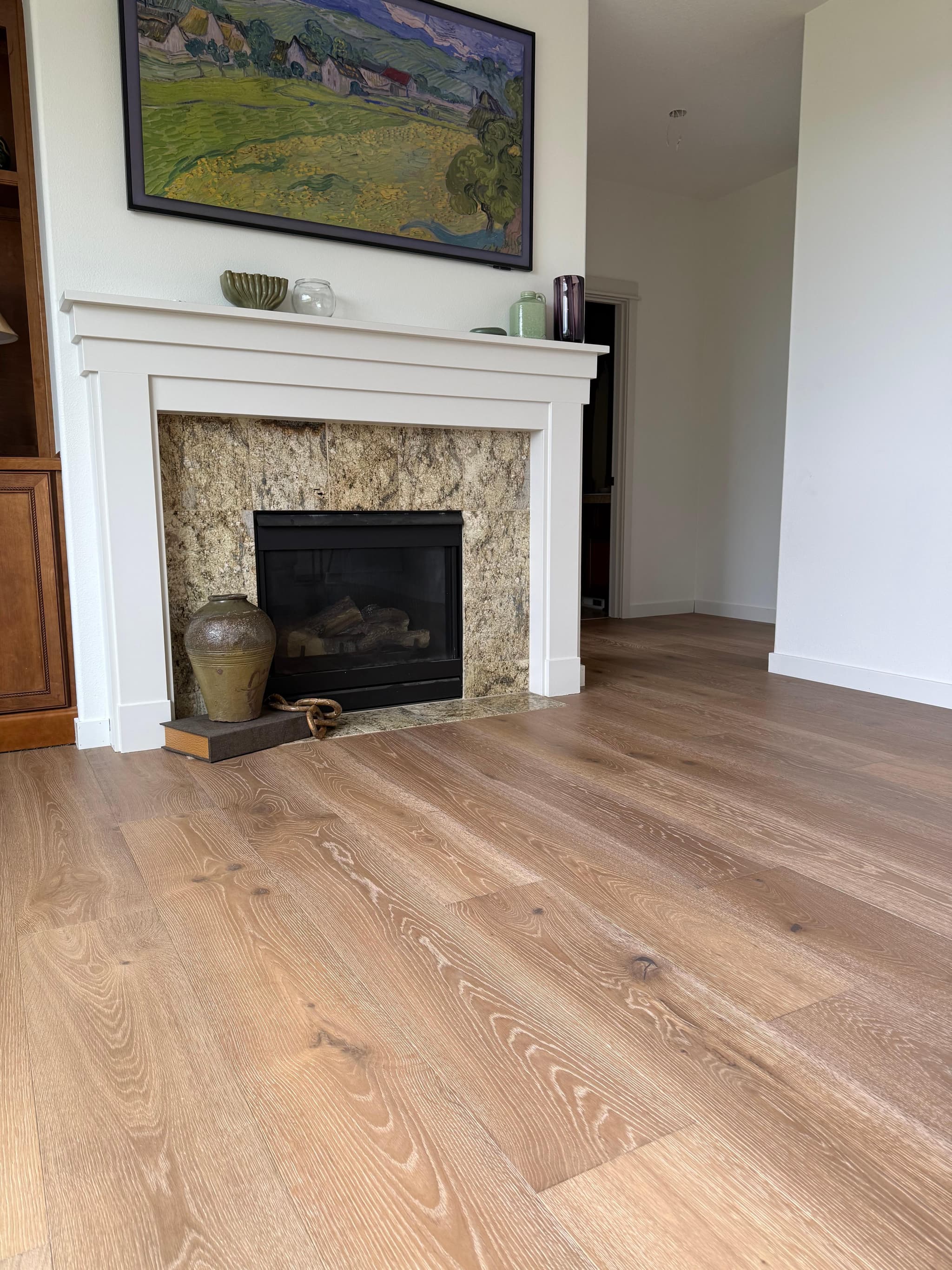 Wide-plank engineered hardwood flooring running up to a white fireplace mantel with a stone surround in a Ridgefield, WA living room