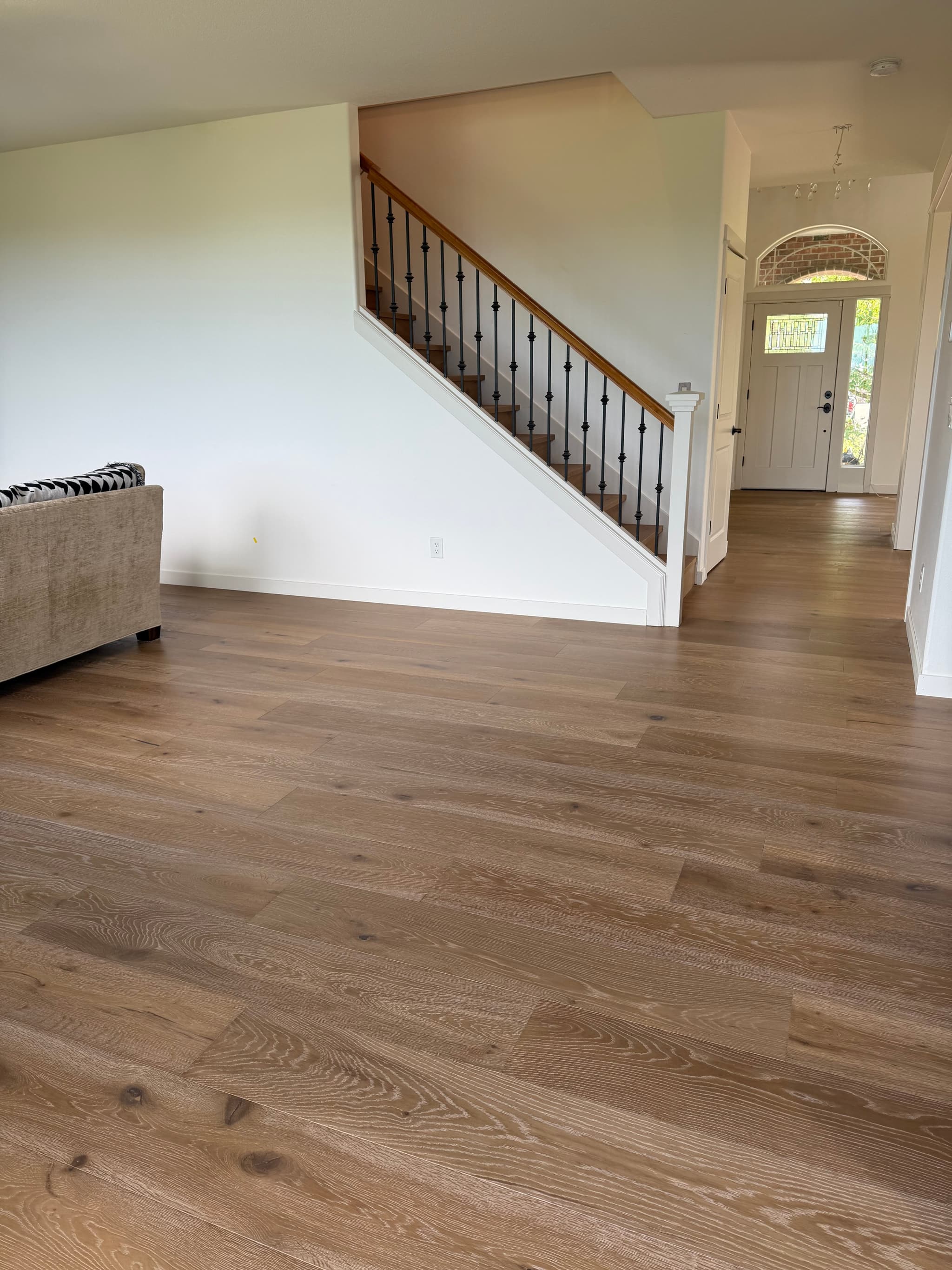 Engineered hardwood flooring installed across an open living room and front entry, with matching oak stair treads and black iron balusters, in a Ridgefield, WA home