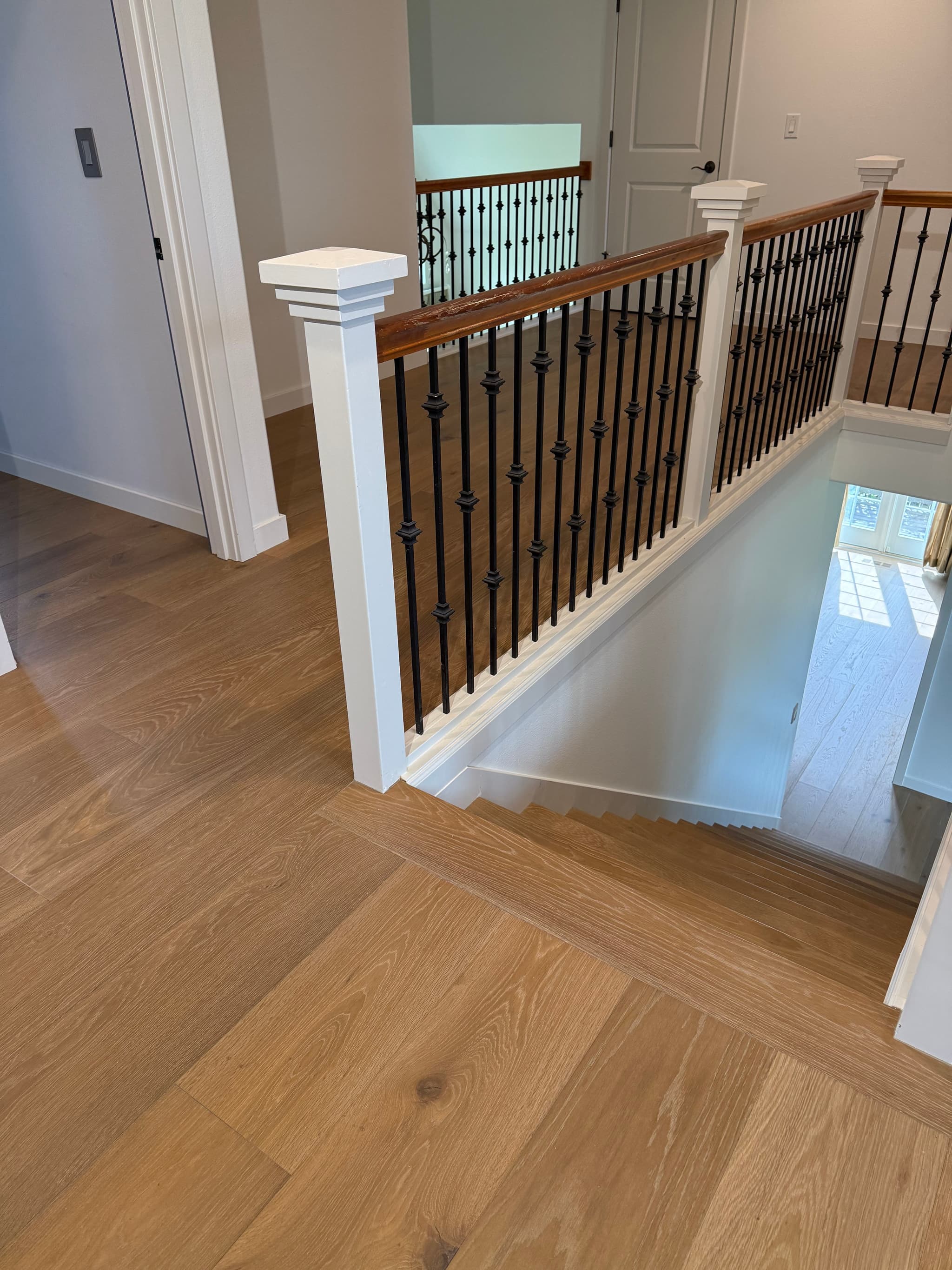 Engineered hardwood flooring on the upper landing of a Ridgefield, WA home with matching oak stair treads descending past a black iron baluster railing
