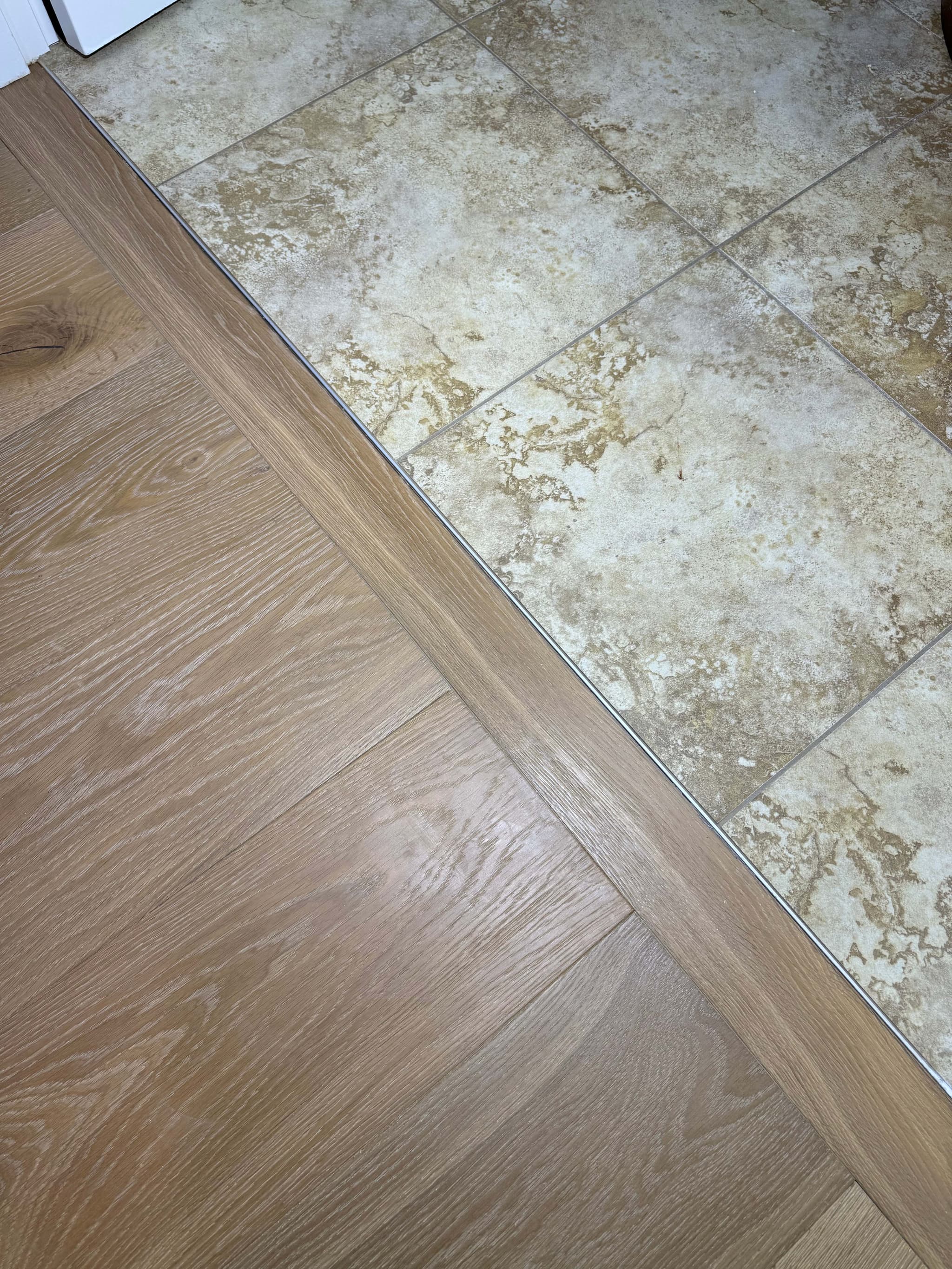 Close-up of a metal transition strip joining engineered hardwood flooring to existing travertine tile in a Ridgefield, WA home